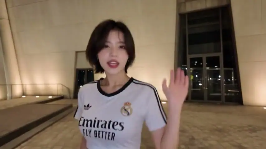 The performer in a white sports jersey reaching toward the camera in front of a building.