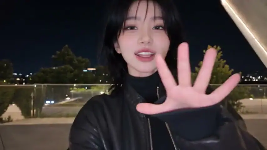 The lead in a black jacket holding an open palm toward the lens.